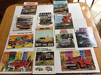 Photo showing twelve vintage GMC truck sales brochures laid out on a table including vans, pickups, 4WD, Jimmy Suburban, Rally Wagon and more from the 1970s.