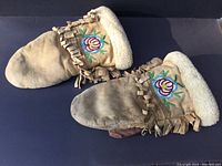 Pair of vintage First Nations handmade mitts with floral beadwork and wool liners laid flat to show full length and wear on leather.