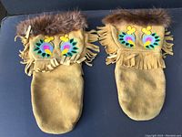 Pair of mitts showing full front, leather base with fringe and colorful beadwork, fur trim around wrist area.