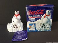 Full view of the Coca Cola Polar Bear mechanical bank with original box and instruction sheet, showing the bear seated on ice with Coca Cola bottles.