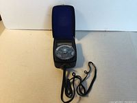 Full view of Gossen Lunasix 3 light meter inside its black case with blue lining, showing attached black cord.
