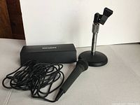 Photo of the Genexxa microphone with attached cable placed next to the Atlas Sound microphone stand with cast base and adjustable holder.