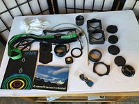 Full view of items showing lens caps, filter holders, adapter rings, lens hood, booklet, camera strap, cleaning cloth, and other camera accessories.