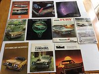 10 vintage car brochures laid flat on a surface, showing front covers with car models and years.
