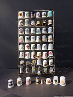 Full view of 48 decorative sewing thimbles displayed on a metal rack plus 8 additional thimbles laid out at the bottom.