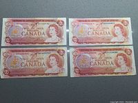 Four Canadian $2 bills from 1974 laid out for viewing, showing both front design and serial numbers