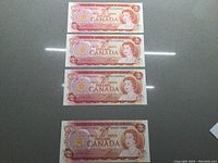 Four Canadian $2 bills displayed face up, showing the portrait of Queen Elizabeth II and denomination details. Three bills have consecutive serial numbers.