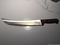 Full view of the large curved carving knife with wooden handle lying on a white surface.