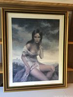 Full view of the framed print showing the artwork of a woman in a torn dress sitting, with a cloudy sky background, in a gold-tone frame with white matting.