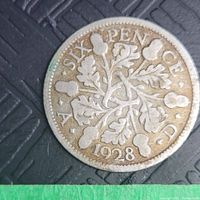 Close-up photo of the reverse side of the 1928 British silver six pence coin showing the denomination, year, and oak leaf design.
