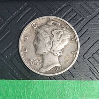 Obverse side of a 1943 US Mercury Dime coin placed on a textured surface, showing wear and tarnish.