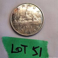 Reverse side of the 1953 Canada Silver Dollar showing Voyageur design with canoe and two indigenous men paddling, 1953 date, CANADA and DOLLAR inscriptions. Coin shows surface wear.