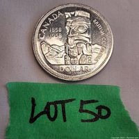 Photo shows the reverse side of the 1958 Canadian silver dollar with detailed British Columbia Totem Pole design, mountain background, and text including dates 1858 and 1958, Canada, British Columbia, and Dollar.