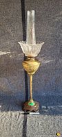 Full view of tall banquet lamp standing on patterned base with brass body and clear glass chimney and shade.