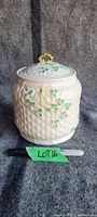 Full front view of cream-colored porcelain biscuit jar with basket weave texture and hand-painted shamrocks on the body with yellow bow detail.