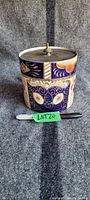 Front view of the cylindrical biscuit jar with English Imari pattern and metal lid with knob.