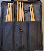 Five sets of wooden drumsticks held in three pouch sections of a black fabric carrying case with Zildjian branding. Some sticks show signatures.