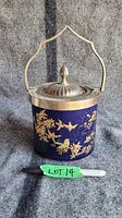 Front view of cobalt blue Limoges biscuit jar with applied gold bird and floral decoration, silver-plated lid with figural finial, and handle.
