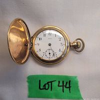 Front view of vintage Omega pocket watch with open face showing dial, minute and second hands but missing hour hand. Green tag labeled Lot 44 visible.