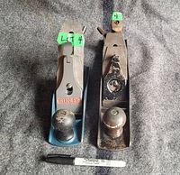 Pair of wood planes with size comparison via marker, one Stanley 8 inch painted blue, one 11 inch made in USA with patina