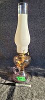 Full view of the pedestal finger oil lamp with a tall white glass chimney, brass burner, and clear glass pedestal base with a handle.