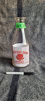 Full view of the glass milk bottle with visible label and overall shape with a marker for scale.