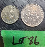 Photo showing both 1 Franc 1969 and 1/2 Franc 1965 French coins on a black background with green tape labeled Lot 86.