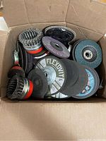 Box open showing mixed grinding wheels including FLEXOVIT branded cutting discs and wire brushes