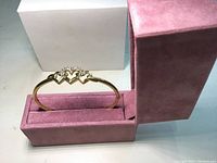 Front view of gold bracelet with three interlocking hearts in pink velvet case.