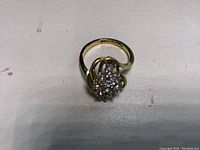 Gold women's ring shown from top front angle, highlighting diamond cluster and band design with some internal stamp visible