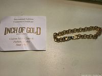 Close-up of the Inch of Gold Guarantee Certificate and part of the gold bracelet chain links.