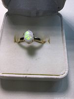 Front-facing image showing the gold ring with an oval white opal gemstone set in a white cushioned box.