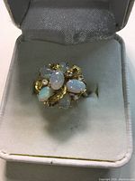 Close-up front view of gold ring with cluster of opal pearls, placed in a white velvet jewelry box.