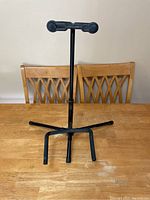 Black metal guitar stand with rubber arms and base supports on a wooden table viewed from front.