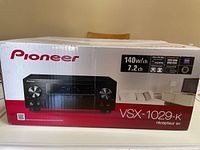Box front showing Pioneer VSX-1029-K receiver details including 140W/channel, 7.2 channel audio, Ultra HD 4K pass-through, Bluetooth, AirPlay, HDMI, and other features.