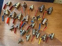 Top down view showing 20 brass plumbing valves with different colored lever handles arranged on a wooden table.