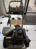Front view of Briggs & Stratton pressure washer showing engine, gas tank, two fluid tanks, wheels, and handle.
