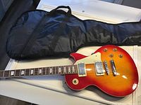 Electric guitar laying on soft case showing full body and part of the neck with sunburst finish and hardware details