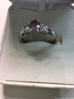 Front angle showing central oval purple gemstone with clear stones on each side, set in silver ring.