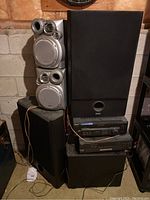 Full view showing 5 speakers stacked and 2 receivers placed between speakers. Speakers include 2 JVC silver face units and 3 black large speakers. Receivers are stacked, Sony on top of Technics.
