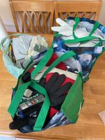 Photo showing three bags on a table filled with various pairs of work gloves of different materials and colors, mostly size large or extra-large.