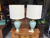 Both matching blue ceramic lamps with white shades placed on a wooden dresser, showing the full assembled appearance.