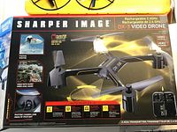 Box with branding and features of the Sharper Image DX-3 rechargeable video drone, showing drone image, camera lens, and flight functions.
