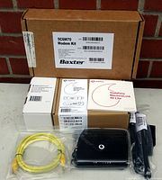 Full kit contents including Baxter labeled cardboard box, user manuals, black Vodafone MachineLink 4G Lite modem/router, yellow Ethernet cable, and power adapter.