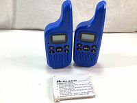 Front view of two blue Midland X-Talker T20 radios with LCD displays, PTT buttons, and other function keys. Small folded quick start guide in front.
