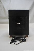 Photo of the subwoofer from rear showing cabinet, wood grain finish, power cord, and one missing leg.