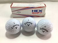 Three Callaway HEX Soft 3 golf balls displayed with their numbered sides showing (2,3,4) alongside the retail box with some visible wear.