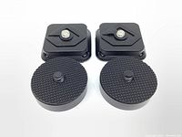Top view of two black square quick release plates and two round converter adapters, arranged in pairs