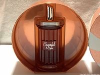 Glass perfume bottle in vertical ridged amber tone with silver cap inside a circular metallic orange gift box