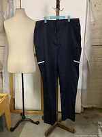 Front view of dark navy blue XXL FedEx work pants displayed on wooden hanger, showing straight leg, cargo pockets with reflective stripes.